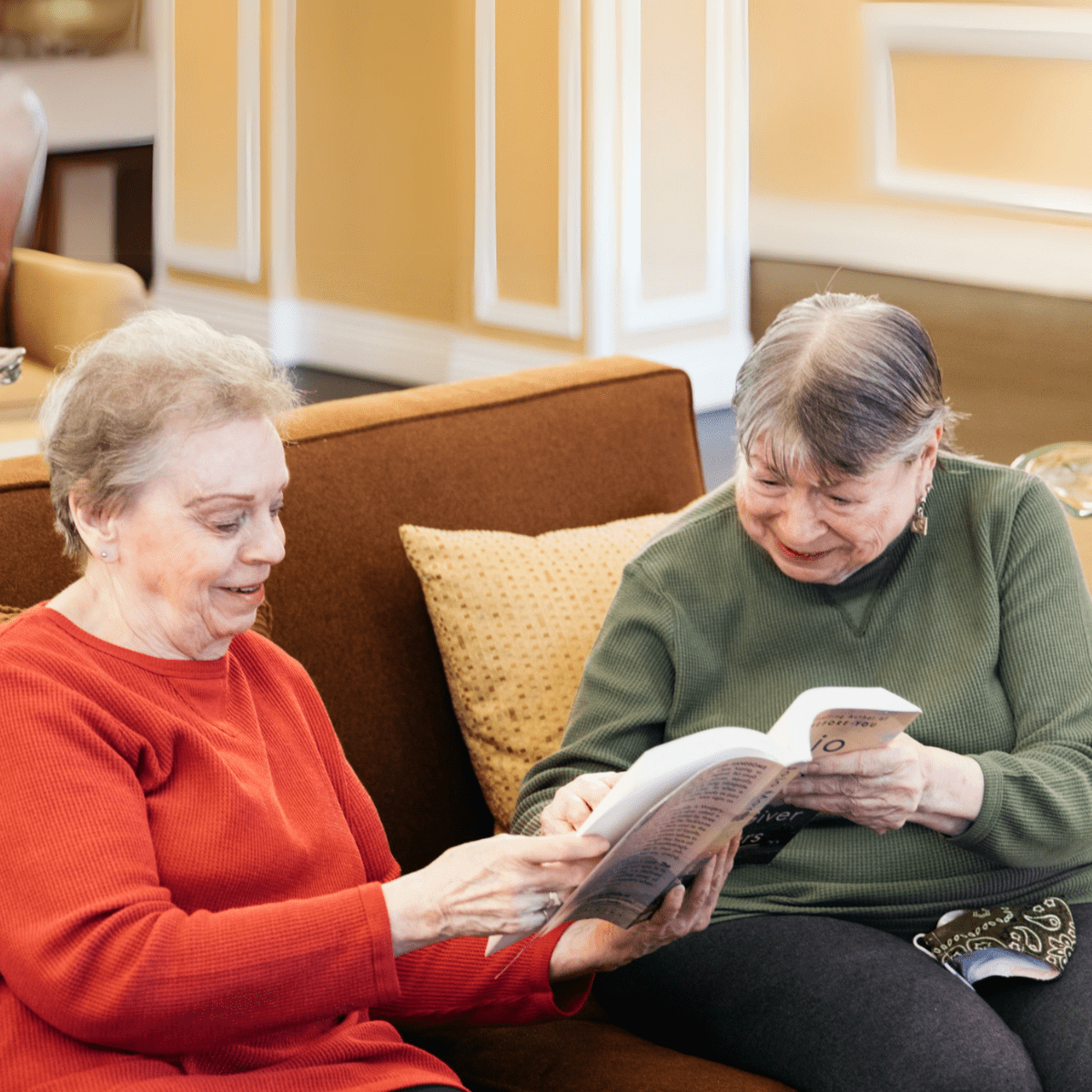 Two Ladies sitting on couch holding book together